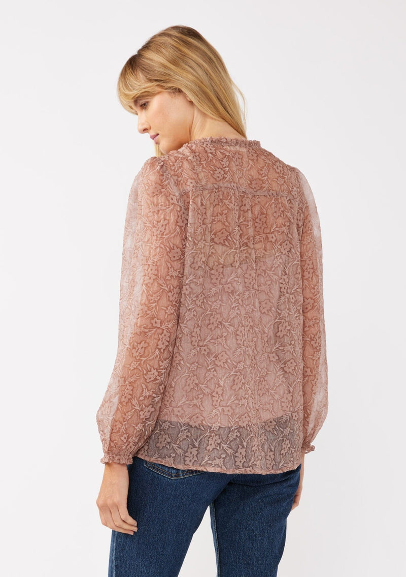 [Color: Mauve] A back facing image of a blonde model wearing a crinkled sheer chiffon blouse with a floral pattern. This relaxed fit blouse features a double tie neck detail, long sleeves with ruffled elastic cuffs, and a detachable cami. 