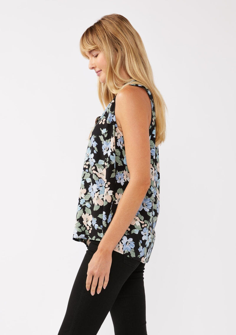 [Color: Black/Pale Blue] A side facing image of a blonde model wearing a black and blue floral print blouse sleeveless top. Featuring a button front and a split v neckline with a ruffle trim detail. Perfect for work and special occasions. 