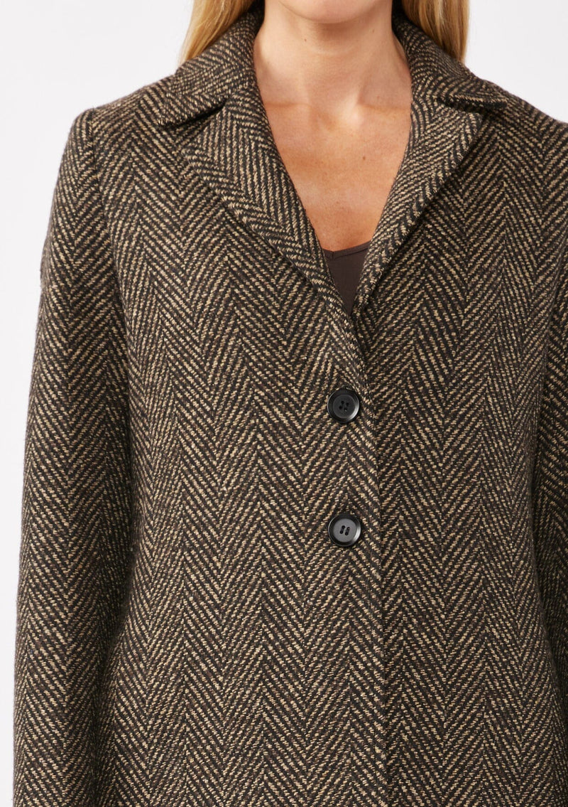 [Color: Brown/Black] A detail image of a blonde model wearing a classic notched lapel coat with a chevron stripe pattern in brown. Featuring a button front and side pockets. The perfect fall staple for any occasion. 