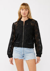 [Color: Black] A front-facing image of a blonde model wearing a black open crochet bomber jacket. The jacket features a floral lace pattern, a zip-up front, and a wide elastic band at the hem and cuffs. This cropped style is perfect for casual outings on vacation or as a beachwear throw on.