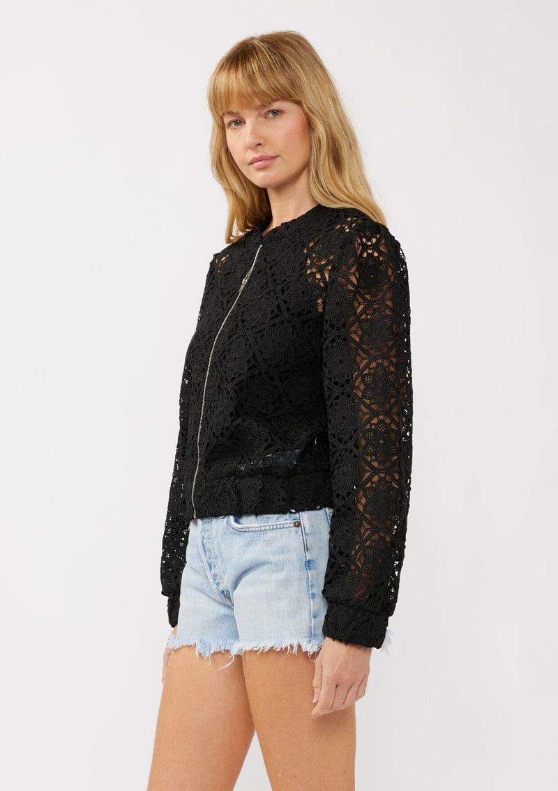 [Color: Black] A side-facing image of a blonde model wearing a black open crochet bomber jacket. The jacket features a floral lace pattern, a zip-up front, and a wide elastic band at the hem and cuffs. This cropped style is perfect for casual outings on vacation or as a beachwear throw on.