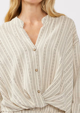 [Color: Natural/Black] A detail image of a blonde model wearing a cotton blend blouse in beige with black yarn-dye stripes. The top features a split V-neckline, button front, front knot, and long sleeves with button tabs, ideal for lounging or vacation style.