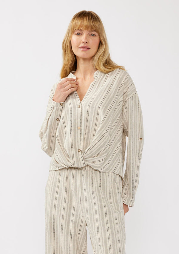 [Color: Natural/Black] A front facing image of a blonde model wearing a cotton blend blouse in beige with black yarn-dye stripes. The top features a split V-neckline, button front, front knot, and long sleeves with button tabs, ideal for lounging or vacation style.