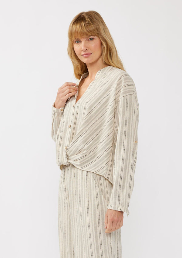 [Color: Natural/Black] A side facing image of a blonde model wearing a cotton blend blouse in beige with black yarn-dye stripes. The top features a split V-neckline, button front, front knot, and long sleeves with button tabs, ideal for lounging or vacation style.