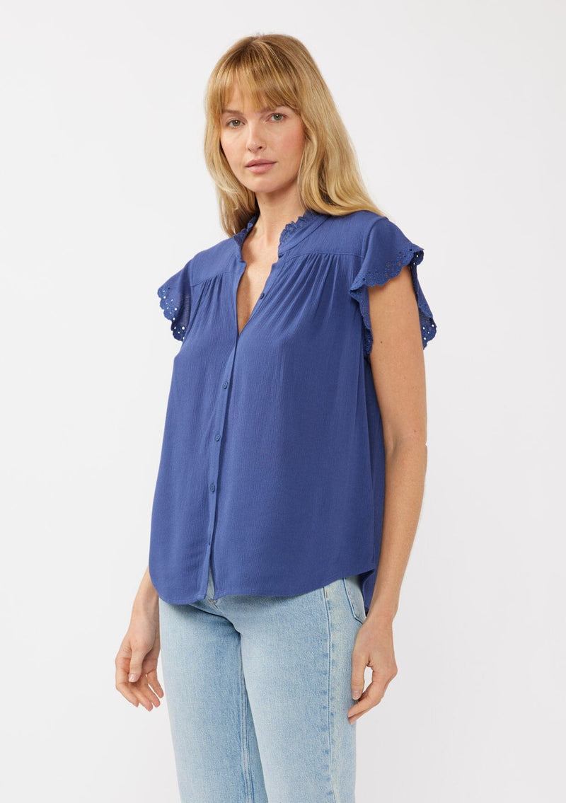 [Color: Ink Blue] A side-facing image of a blonde model wearing a light yellow crinkled rayon top. The top features flutter sleeves with eyelet details, a split V-neckline, and a button-front design, offering a versatile look for everyday wear.