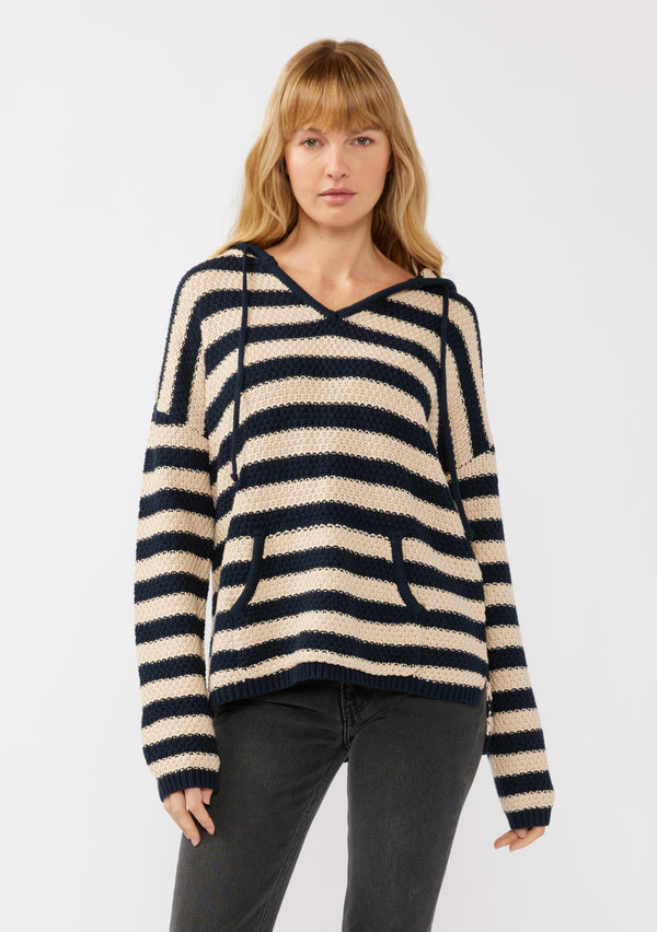 [Color: Navy/Natural] A front facing image of a blonde model wearing a navy and beige striped knit hoodie. With long sleeves, a dropped shoulder, a v neckline, and a front kangaroo pocket. 