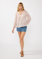 [Color: Natural/Dusty Pink] A front facing image of a blond model wearing a classic v-neck bohemian blouse with a pink abstract print, smocked neckline and cuffs, and button front. 