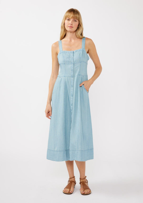 [Color: Light Wash] A front facing image of a blonde model in a blue denim-like Tencel midi dress, showcasing a square neckline, adjustable button-tab straps, button-front design, and handy side pockets—ideal for casual strolls, vacation days, or refined resort style.