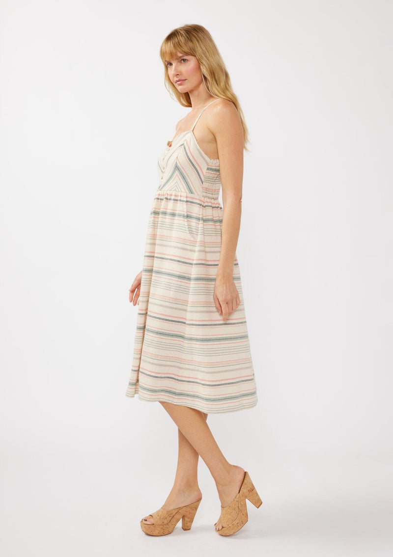 [Color: Natural/Multi] A blonde model wearing a striped yarn-dye midi dress made from lightweight, airy cotton. The dress features a fitted bodice with button details, a smocked back, a full skirt, and side pockets—perfect for casual special occasions.