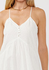 [Color: White] A detail image of a blonde model wearing a bohemian-inspired white maxi dress featuring embroidered eyelet details and textured clip dots. The relaxed, tiered silhouette includes adjustable straps, a v-neckline, and a racerback design, making it ideal for beach days, weddings, or any special occasion.