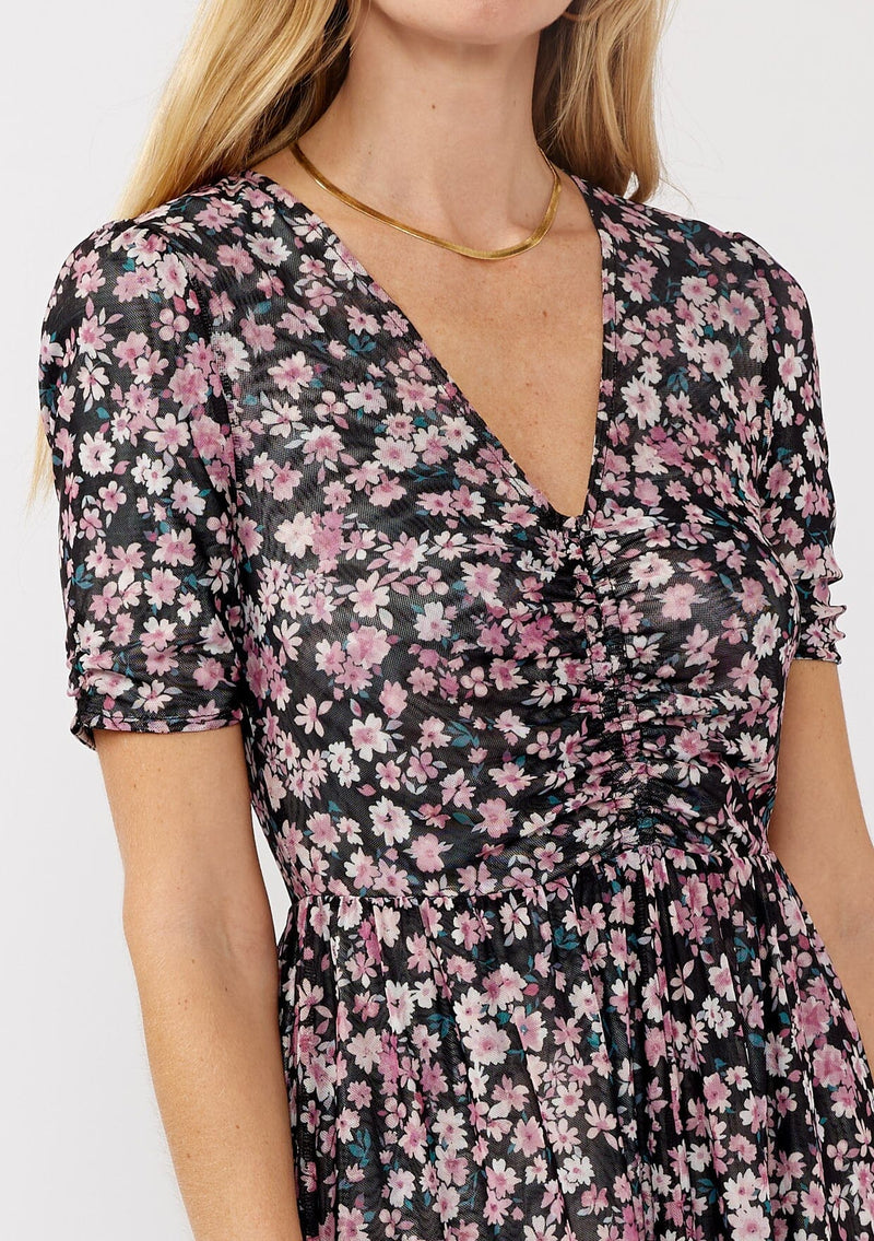 [Color: Black/Dusty Pink] A detail image of a blonde model wearing a soft micro mesh reversible midi dress with pink floral print. Featuring a v-neckline, short sleeves, ruched bust, and a merrow edge hem. Perfect for spring styling and casual days. 