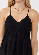 [Color: Black] A detail image of a blonde model wearing a bohemian-inspired black maxi dress featuring embroidered eyelet details and textured clip dots. The relaxed, tiered silhouette includes adjustable straps, a v-neckline, and a racerback design, making it ideal for beach days, weddings, or any special occasion.