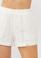 [Color: White] A detail image of a model wearing a white stripe embroidered eyelet short with an elastic waistband and side pockets. Perfect for resort or vacation styling. 