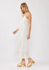 [Color: White] A side image of a blonde model wearing a bohemian-inspired white maxi dress featuring embroidered eyelet details and textured clip dots. The relaxed, tiered silhouette includes adjustable straps, a v-neckline, and a racerback design, making it ideal for beach days, weddings, or any special occasion.