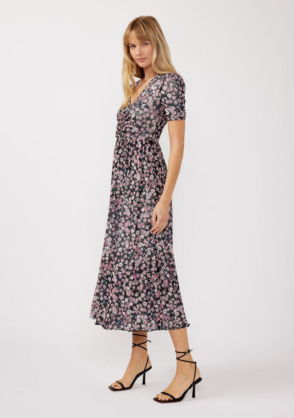 [Color: Black/Dusty Pink] A side facing image of a blonde model wearing a soft micro mesh reversible midi dress with pink floral print. Featuring a v-neckline, short sleeves, ruched bust, and a merrow edge hem. Perfect for spring styling and casual days. 