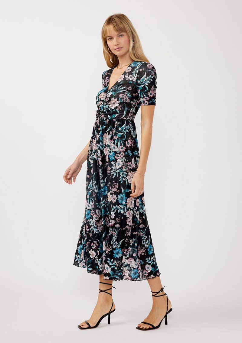 [Color: Black/Dusty Pink] A side facing image of a blonde model wearing a soft micro mesh reversible midi dress with blue floral print. Featuring a v-neckline, short sleeves, ruched bust, and a merrow edge hem. Perfect for spring styling and casual days. 