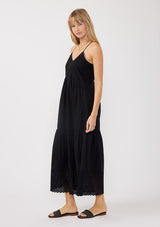 [Color: Black] A side image of a blonde model wearing a bohemian-inspired black maxi dress featuring embroidered eyelet details and textured clip dots. The relaxed, tiered silhouette includes adjustable straps, a v-neckline, and a racerback design, making it ideal for beach days, weddings, or any special occasion.