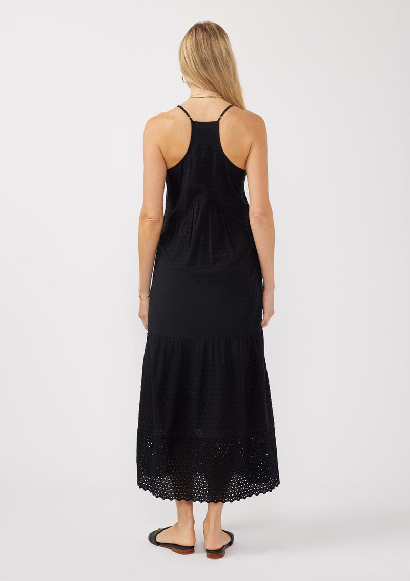 [Color: Black] A back image of a blonde model wearing a bohemian-inspired black maxi dress featuring embroidered eyelet details and textured clip dots. The relaxed, tiered silhouette includes adjustable straps, a v-neckline, and a racerback design, making it ideal for beach days, weddings, or any special occasion.