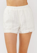 [Color: White] A front facing image of a  model wearing a white stripe embroidered eyelet short with an elastic waistband and side pockets. Perfect for resort or vacation styling. 