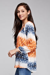 [Color: Coral/Navy] A brunette model wearing a tie dye blouse with paisley print in orange and blue. With a scoop neckline, long sleeves, and button front. A relaxed fit style paired with denim jeans.