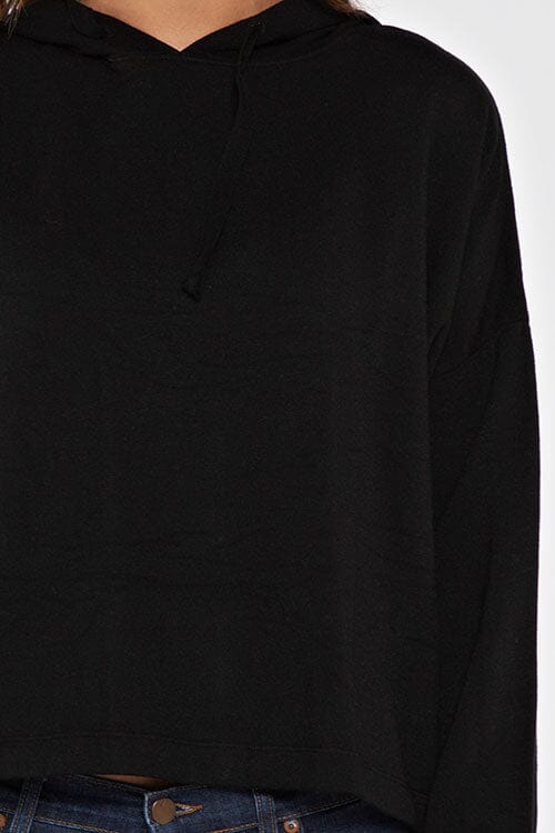 [Color: Black]  A brunette model wearing a solid black pullover hoodie with a drawstring hood, long sleeves, and dropped shoulders. The cropped length makes it perfect for lounging, travel, or casual fall outings.