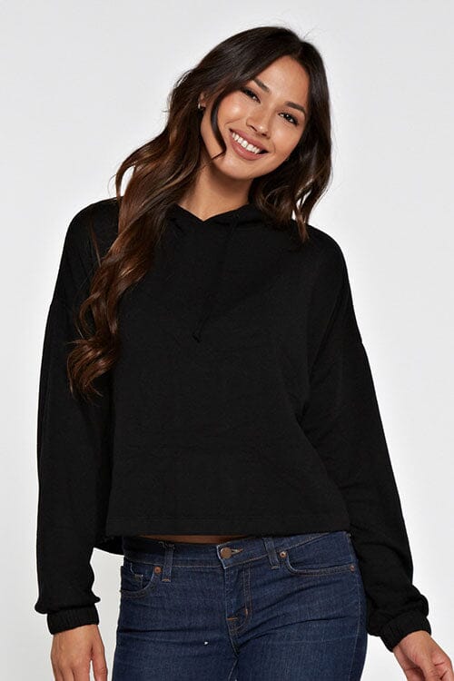 [Color: Black]  A brunette model wearing a solid black pullover hoodie with a drawstring hood, long sleeves, and dropped shoulders. The cropped length makes it perfect for lounging, travel, or casual fall outings.