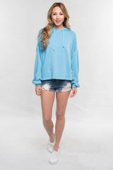 [Color: Cool Blue]  A blonde model wearing a solid blue pullover hoodie with a drawstring hood, long sleeves, and dropped shoulders. The cropped length makes it perfect for lounging, travel, or casual fall outings.