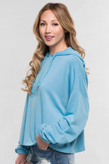 [Color: Cool Blue]  A blonde model wearing a solid blue pullover hoodie with a drawstring hood, long sleeves, and dropped shoulders. The cropped length makes it perfect for lounging, travel, or casual fall outings.