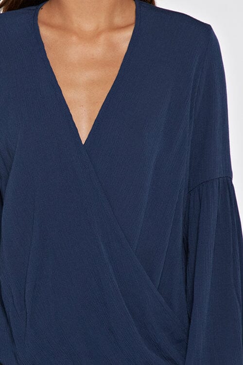 [Color: Deep Blue] A blonde model wearing a blue surplice v neckline blouse with long voluminous sleeves. Complete with a tassel tie detail on the cuff. Perfectly relaxed and ultra boho for any season. 