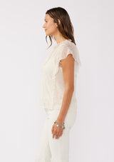 [Color: Ivory] A side facing image of a brunette model wearing a crinkled chiffon top with a floral pattern. This ivory off white top features a sheer flowy silhouette, flutter short sleeves, split v neckline with ties, and ruffled details with a merrow edge finish.  