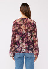 [Color: Plum/Dusty Rose] A back facing image of a brunette model wearing a sheer purple floral chiffon blouse. The blouse features tiered long bell sleeves and a ruffled split v-neckline with tie details. Perfect for day-to-night outings and special occasions in the Fall season. 