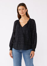 [Color: Black] A brunette model wearing a black peasant top in a jacquard stripe with metallic lurex details. Featuring a classic split neckline with tie detail, long sleeves, smocked cuffs, and a flowy, relaxed silhouette. An elevated casual peasant top, perfect for any holiday celebration or nice dinners.