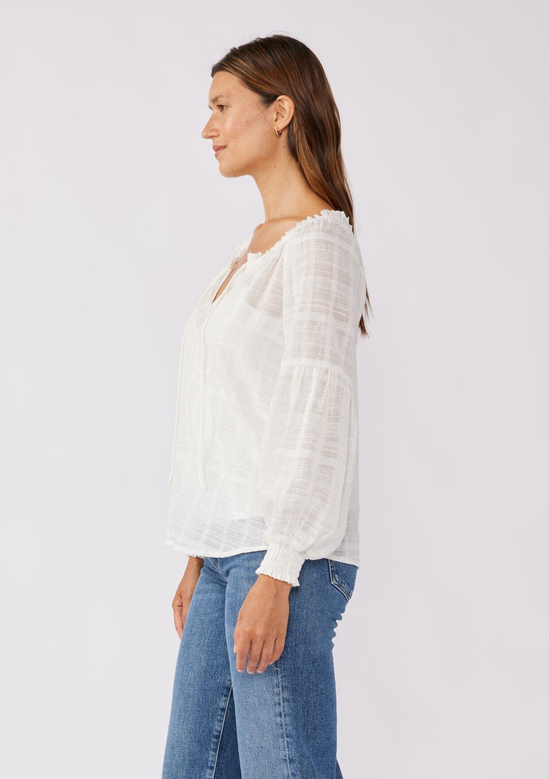 [Color: White] A brunette model wearing a white peasant top in a jacquard stripe with metallic lurex details. Featuring a classic split neckline with tie detail, long sleeves, smocked cuffs, and a flowy, relaxed silhouette. An elevated casual peasant top, perfect for any holiday celebration or nice dinners.