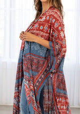 [Color: Blue/Brick] A model wearing a red and blue bohemian mid length kimono. Featuring half length kimono sleeves, side slits, an open front, and a multi colored bohemian pattern throughout.