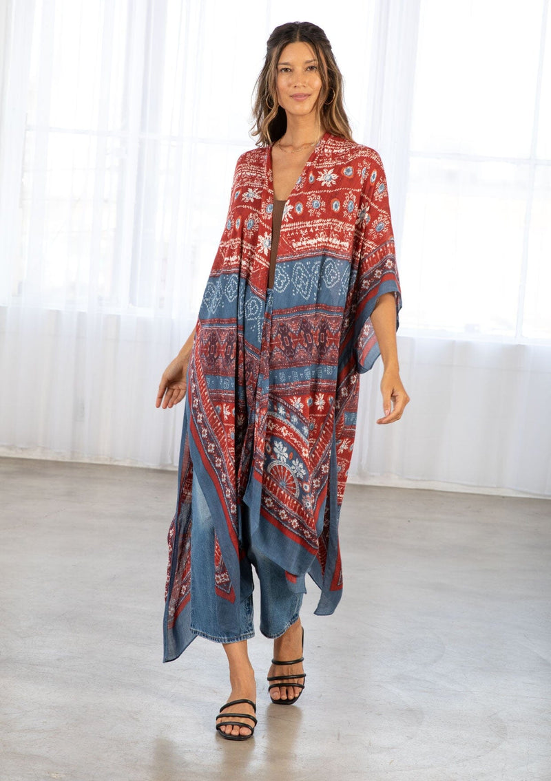 [Color: Blue/Brick] A model wearing a red and blue bohemian mid length kimono. Featuring half length kimono sleeves, side slits, an open front, and a multi colored bohemian pattern throughout.