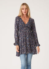 [Color: Navy/Tan] A front facing image of a blonde model wearing a navy blue and tan paisley print tunic top. A vintage inspired top with long sleeves, a smocked bodice, an empire waist, and a deep v neckline.