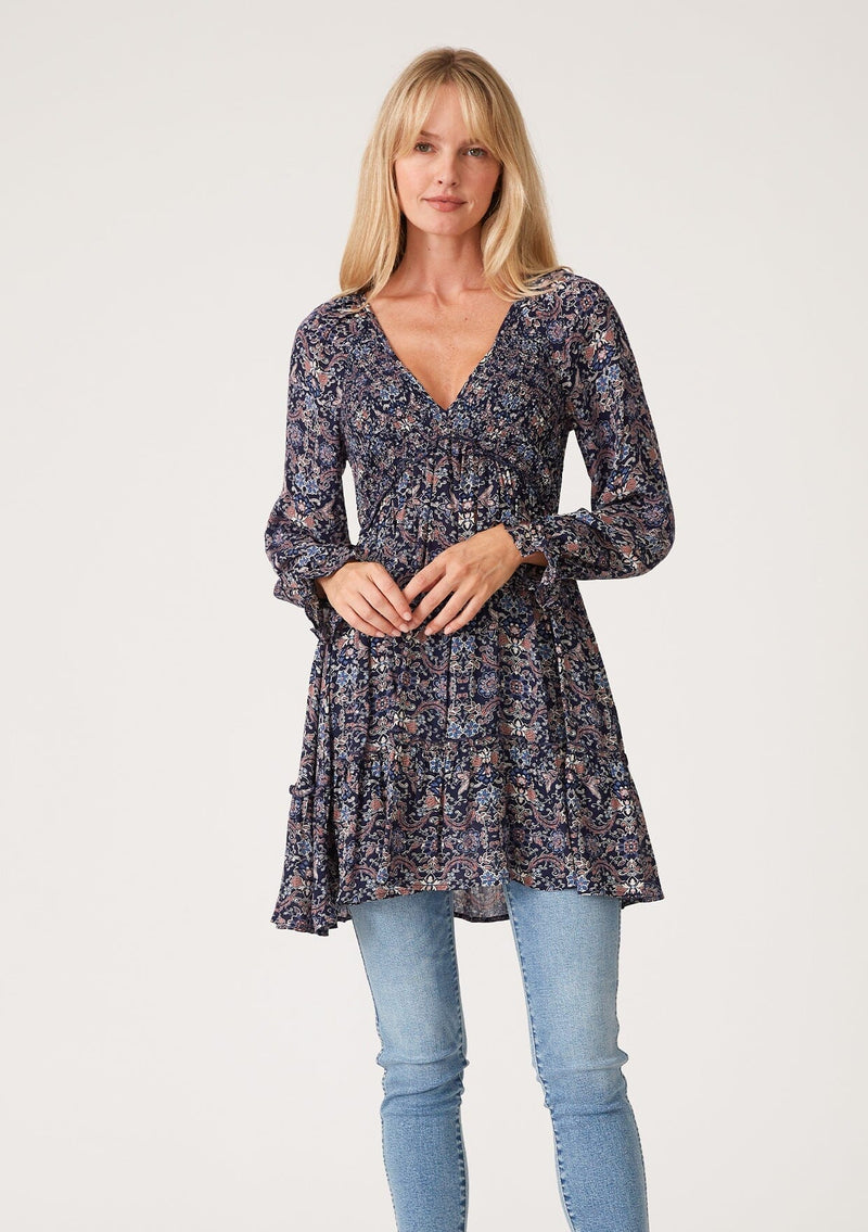 [Color: Navy/Tan] A front facing image of a blonde model wearing a navy blue and tan paisley print tunic top. A vintage inspired top with long sleeves, a smocked bodice, an empire waist, and a deep v neckline.