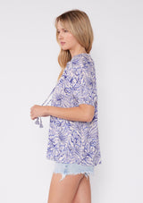 [Color: Bone/Lilac] Beautiful image of short sleeve white bohemian blouse with purple botanical print and a split v-neckline with tassel ties. A cute summer blouse with a relaxed fit.