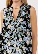 [Color: Black/Pale Blue]A detail image of a blonde model wearing a black and blue floral print blouse sleeveless top. Featuring a button front and a split v neckline with a ruffle trim detail. Perfect for work and special occasions. 