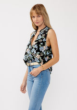 [Color: Black/Pale Blue] A side facing image of a blonde model wearing a black and blue floral print blouse sleeveless top. Featuring a button front and a split v neckline with a ruffle trim detail. Perfect for work and special occasions. 