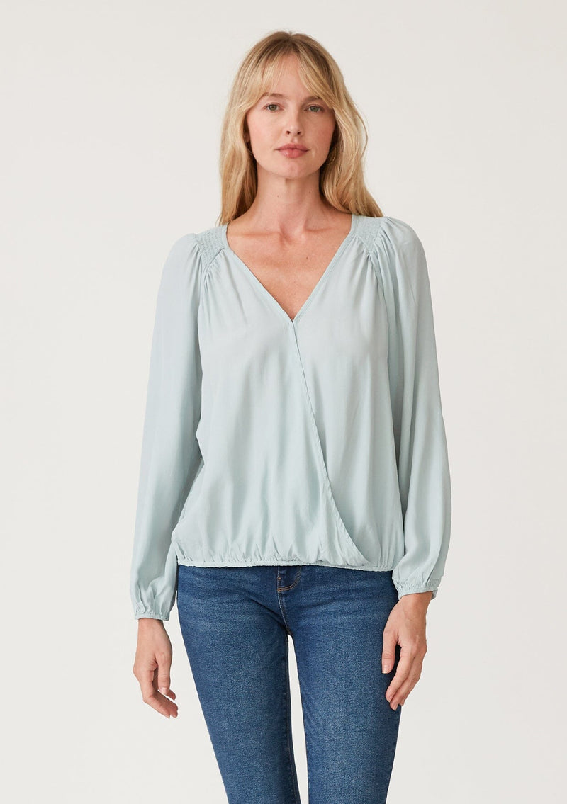 [Color: Sky] A front facing image of a blonde model wearing a soft and silky light blue bohemian blouse with voluminous long sleeves, a plunging surplice v neckline, and an elastic front waist.