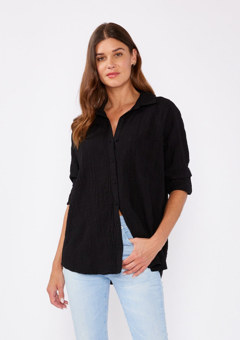 [Color: Black] Brunette woman wearing an olive green plaid seersucker shirt with a button front, roll tab long sleeve, collared neckline. A great top to pair with denim pants or shorts.