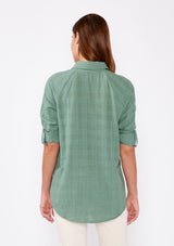 [Color: Dusty Olive] Brunette woman wearing an olive green plaid seersucker shirt with a button front, roll tab long sleeve, collared neckline. A great top to pair with denim pants or shorts.