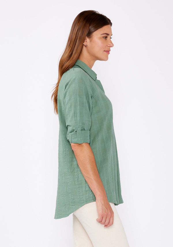 [Color: Dusty Olive] Brunette woman wearing an olive green plaid seersucker shirt with a button front, roll tab long sleeve, collared neckline. A great top to pair with denim pants or shorts.