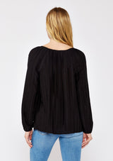 [Color: Black] A back facing image of a blonde model wearing a bohemian black blouse with embroidered details. With long raglan sleeves, a round neckline with a single button closure, a front keyhole, and a relaxed fit.