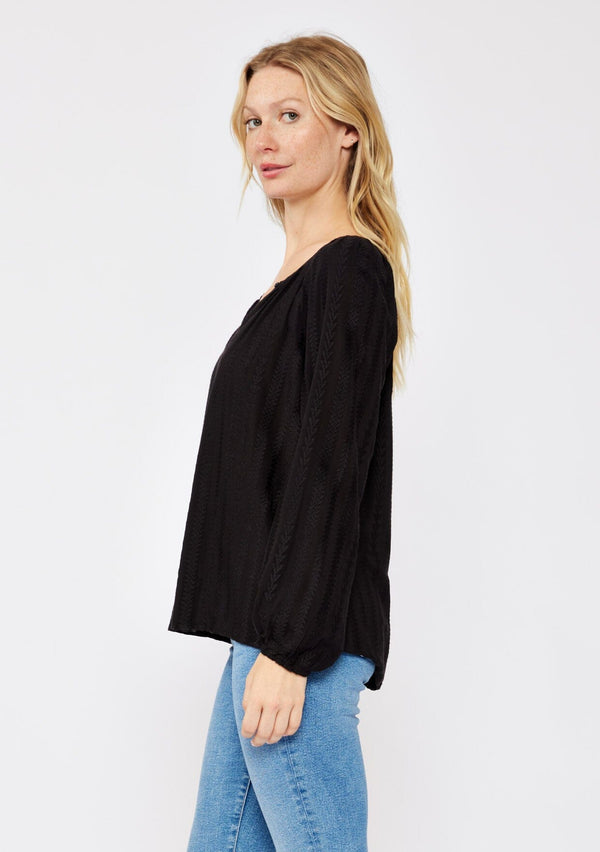 [Color: Black] A side facing image of a blonde model wearing a bohemian black blouse with embroidered details. With long raglan sleeves, a round neckline with a single button closure, a front keyhole, and a relaxed fit.