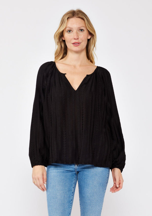 [Color: Black] A front facing image of a blonde model wearing a bohemian black blouse with embroidered details. With long raglan sleeves, a round neckline with a single button closure, a front keyhole, and a relaxed fit.