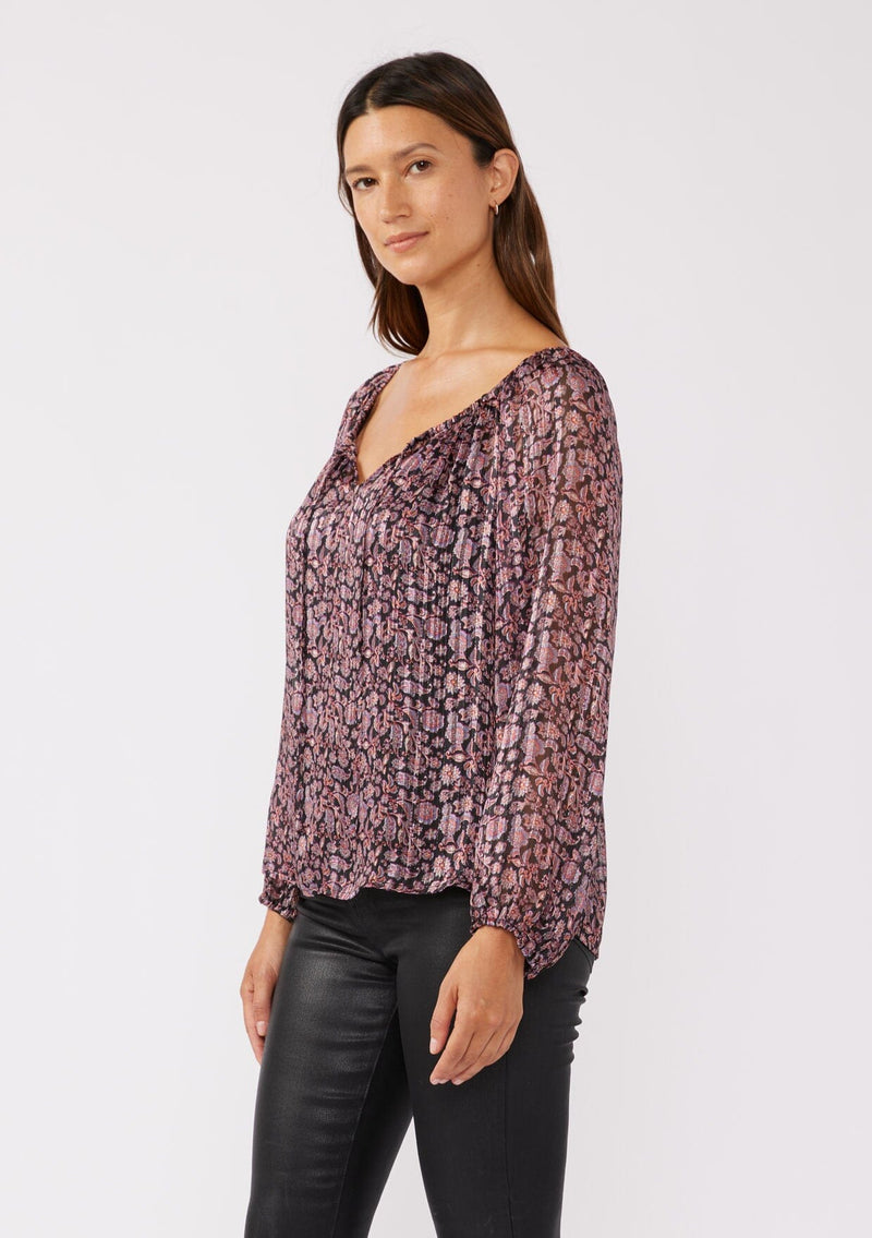 [Color: Black/Plum] A side facing image of a brunette model wearing sheer lurex stripe top with a standout purple floral print. This holiday blouse features long sleeves, elastic cuffs, and a scoop neckline with a tie front detail. Elegantly styled for the holiday season and special occasions. 