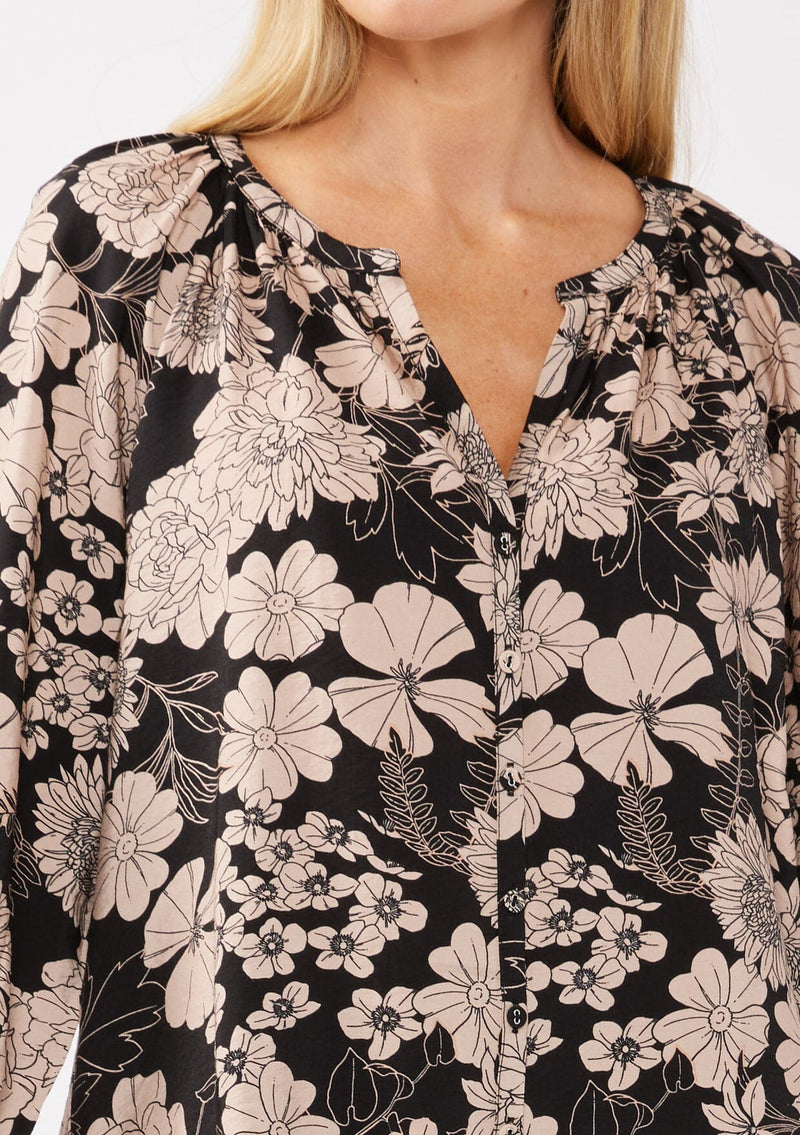 [Color: Black/Taupe] A detail image of a blonde model wearing a black and taupe floral print blouse. This boho casual blouse features a self covered button front, a split v-neckline, and 3/4 length sleeves. Perfect for any casual outing or vacation. 