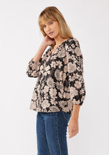 [Color: Black/Taupe] A side facing image of a blonde model wearing a black and taupe floral print blouse. This boho casual blouse features a self covered button front, a split v-neckline, and 3/4 length sleeves. Perfect for any casual outing or vacation. 